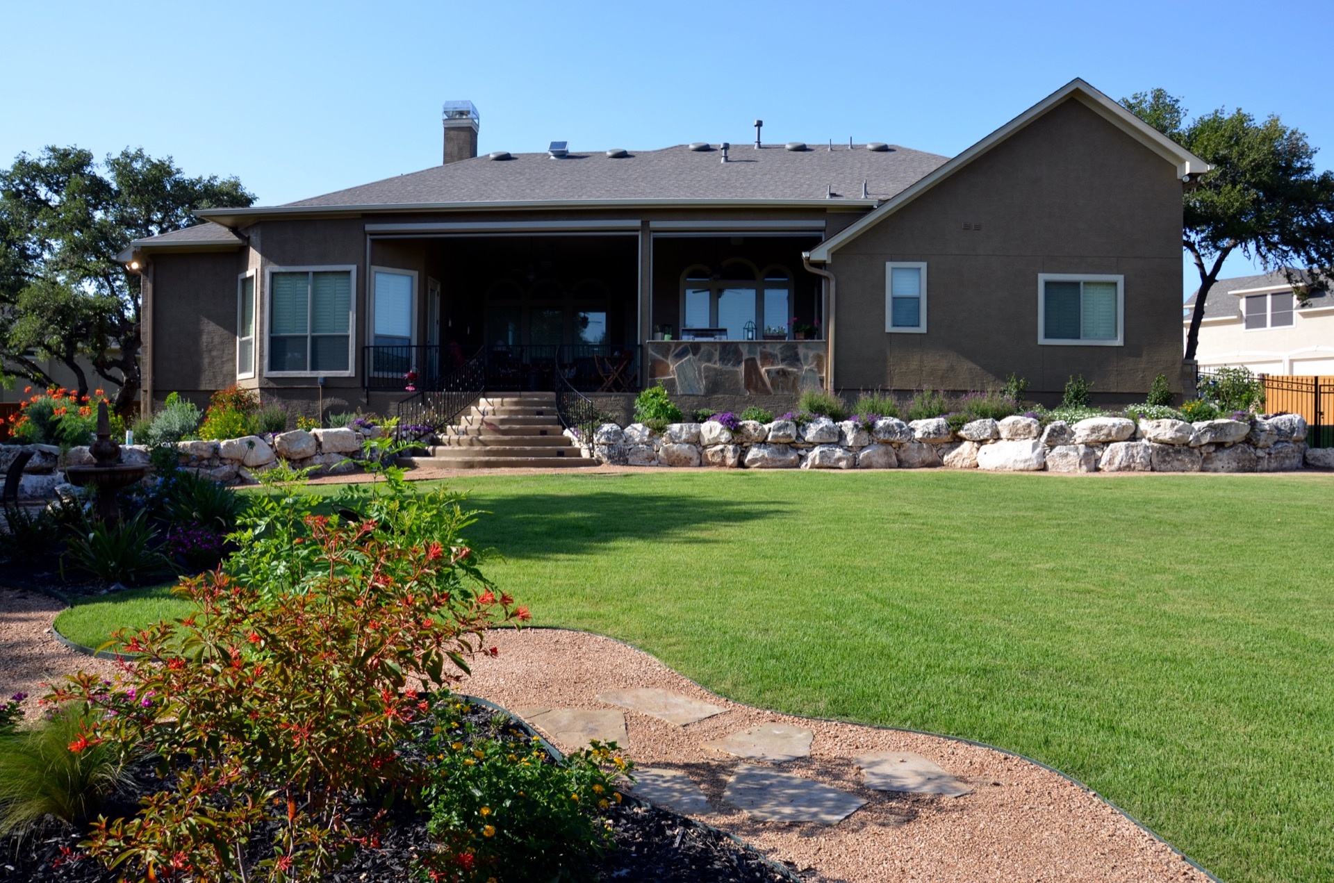 Manicured backyard lawn with stone retaining wall and flower beds, San Antonio